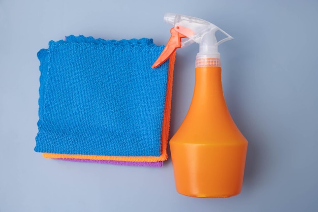 Em um fundo azul, um pulevizador laranja fica ao lado da vista superior dos panos de limpeza de microfibra