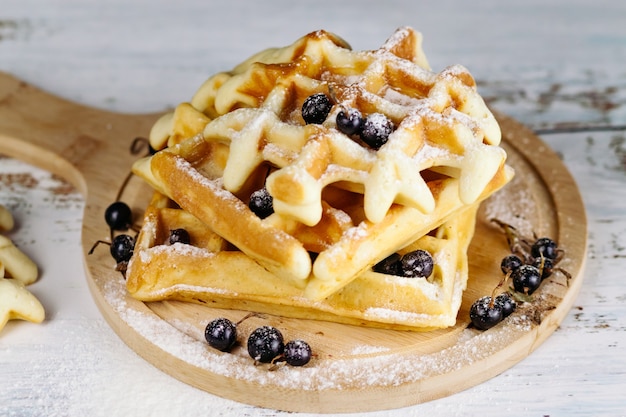 Em um fundo claro, waffles vienenses são empilhados em uma placa redonda, um a um. Waffles dourados são decorados com groselhas negras.