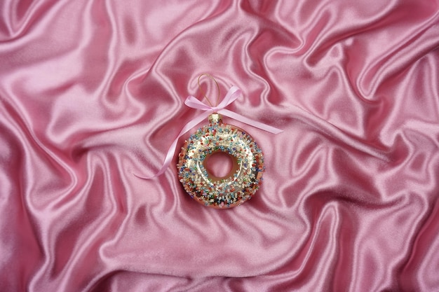 Em um fundo de seda rosa há um brinquedo de árvore de Natal na forma de um donut doce