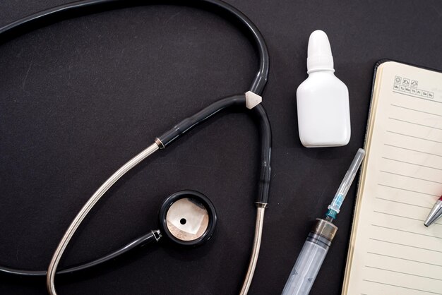 Em um fundo preto é um estetoscópio nariz gotas seringa notebook e caneta conceito de medicina