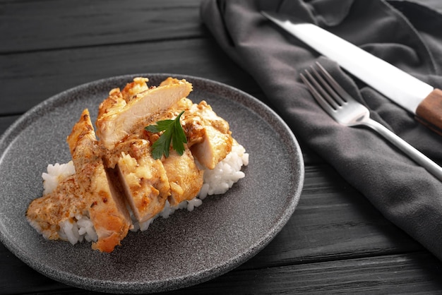 Em um molho cremoso um peito de frango com arroz cortado em pedaços sobre um fundo escuro em um prato cinza Ao lado está uma faca e um garfo Feito em casa