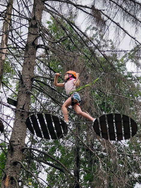 Em um parque de cordas suspensas, um adolescente sobe entre árvores em um obstáculo pendurado
