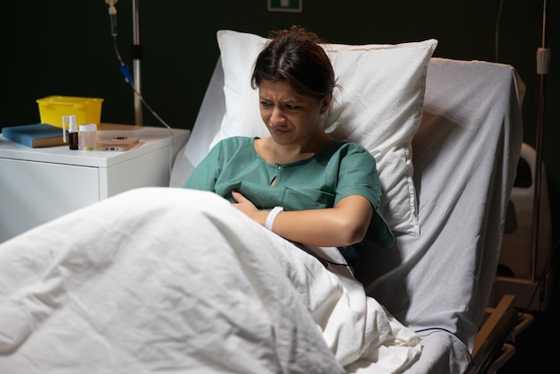 Foto em um quarto de hospital, uma menina vestida com roupas especializadas deita-se agarrando visivelmente o abdômen