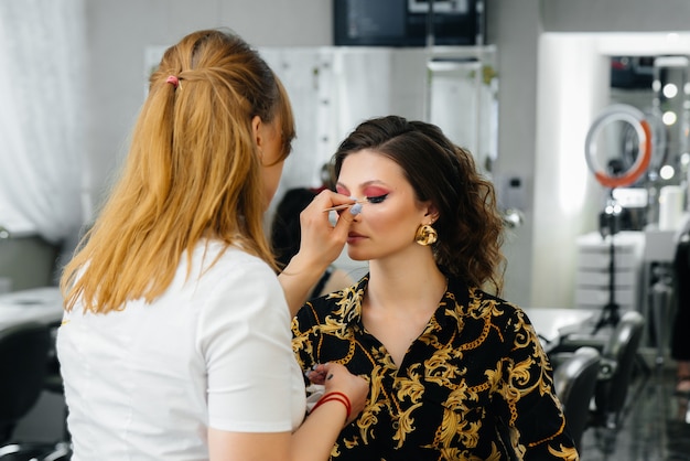 Em um salão de beleza moderno, um estilista de maquiagem profissional faz maquiagem para uma jovem