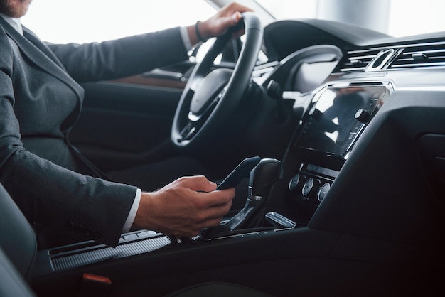 Em um terno preto clássico. Empresário moderno experimentando seu novo carro no salão automóvel.