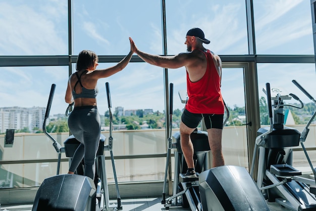 Em uma academia de ginástica, um homem e uma mulher determinados, ambos vestindo trajes esportivos, compartilham um momento triunfante