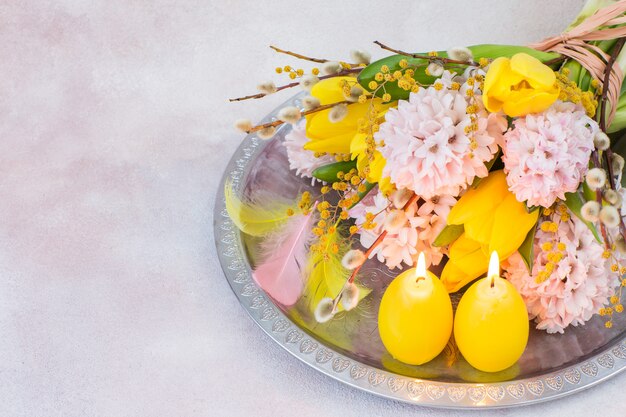 em uma bandeja de prata um buquê de jacintos e tulipas, duas velas em forma de ovos, penas