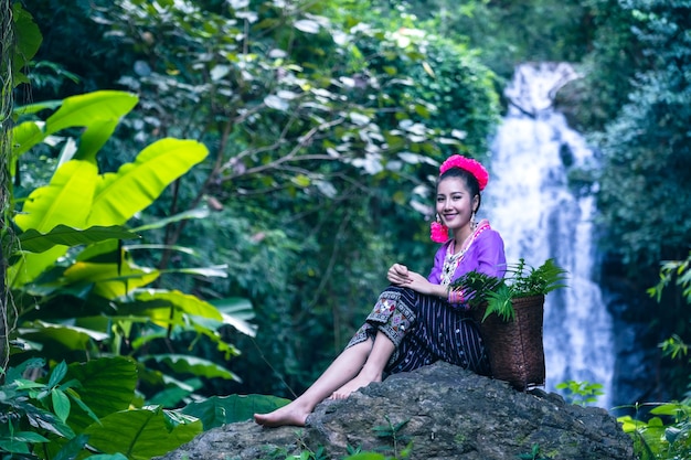 Em uma cachoeira de um rio na zona rural da Tailândia, uma jovem usa uma coroa de flores em uma rocha.