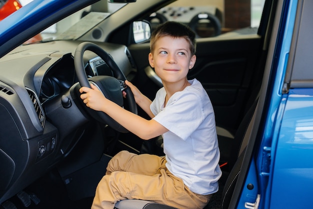 Em uma concessionária de automóveis, um menino feliz está dirigindo um carro novo. compra de carro.