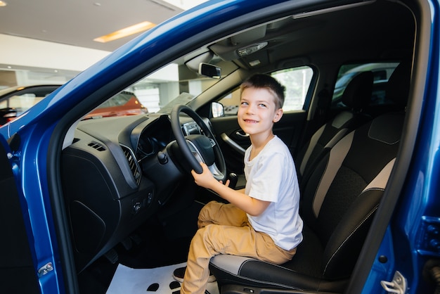 Em uma concessionária de automóveis, um menino feliz está dirigindo um carro novo. compra de carro.