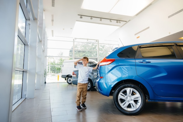 Em uma concessionária de automóveis, um menino feliz fica perto de um carro novo antes de comprá-lo