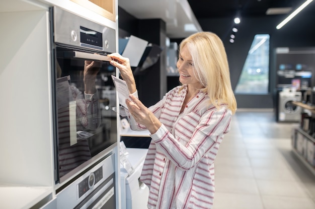 Em uma loja. cliente loira parecendo envolvida ao escolher o forno em um showroom