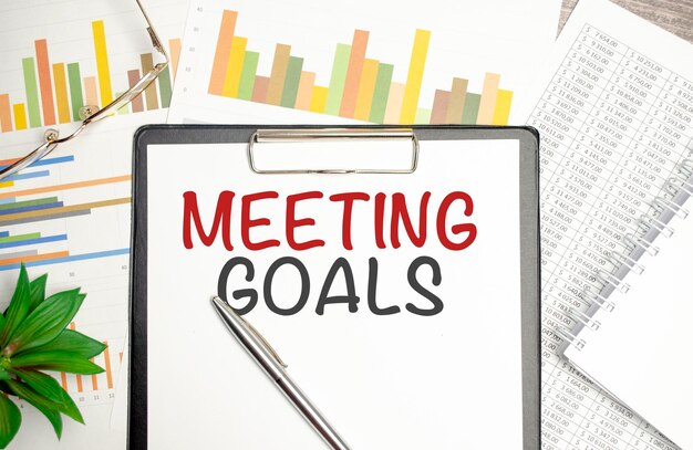 Em uma lupa de fundo de gráfico uma caneta e uma folha de papel com o texto meeting goals
