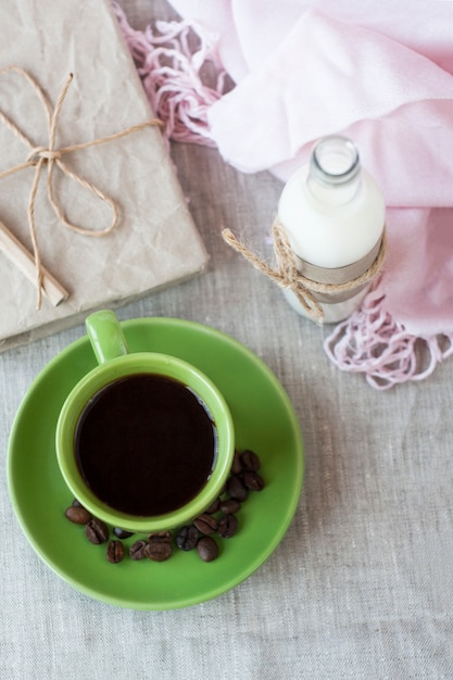 Em uma mesa de luz, há uma xícara de café e uma garrafa de leite. Em seguida é um caderno de artesanato e um guardanapo rosa.