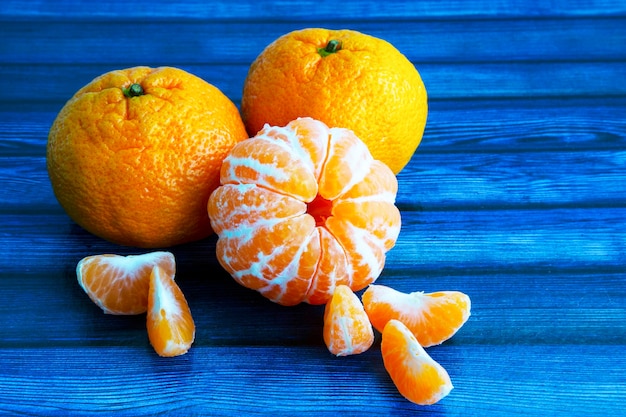 Em uma mesa de madeira azul. tangerinas na pele e sem pele. fatias de tangerina descascada. frutas cítricas