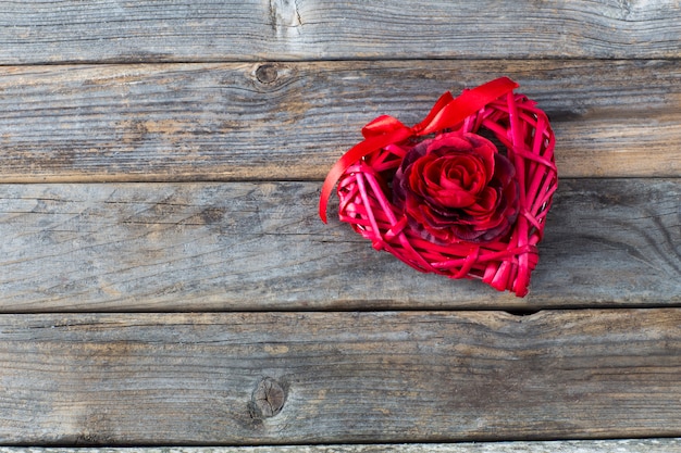 Em uma mesa de madeira, um coração vermelho e um broto de uma rosa vermelha