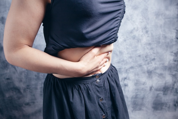 Em uma mulher jovem, seu estômago dói em um fundo cinza