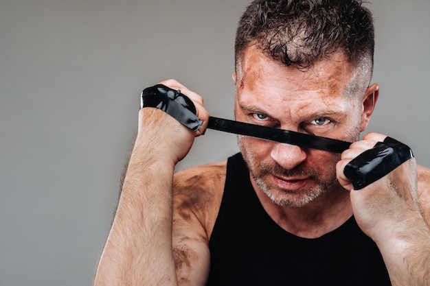 Em uma parede cinza, um homem espancado em uma camiseta preta parecendo um lutador e se preparando para uma luta