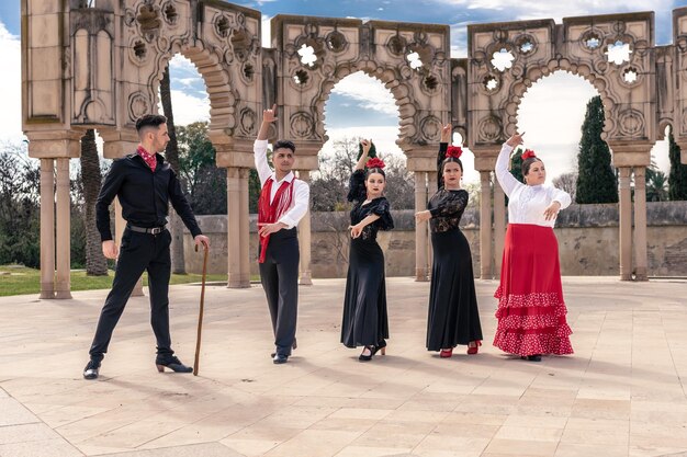 Em uma praça em frente a alguns arcos ornamentais um mestre de flamenco instrui seus aprendizes flamenco