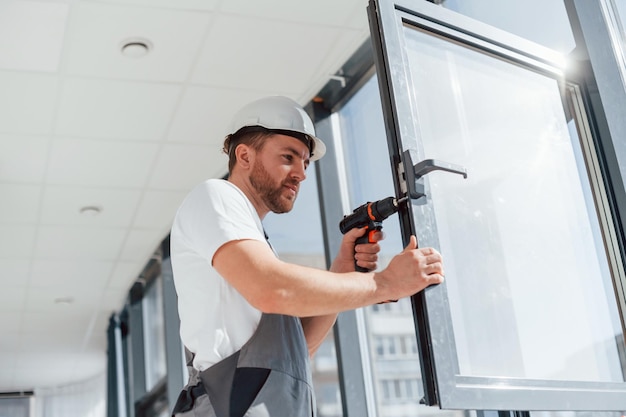 Em uniforme cinza Reparador está trabalhando dentro de casa na sala moderna