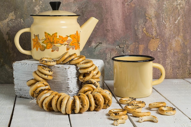 Emaillierte Retro-Teekanne und Becher mit teetrockenen kleinen Bagels auf altem Holztisch