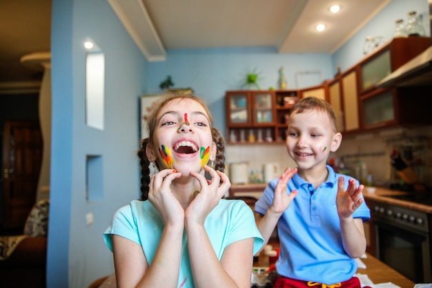 Embadurnado en pintura niños un niño y una niña tonteando y riendo en casa en la cocina