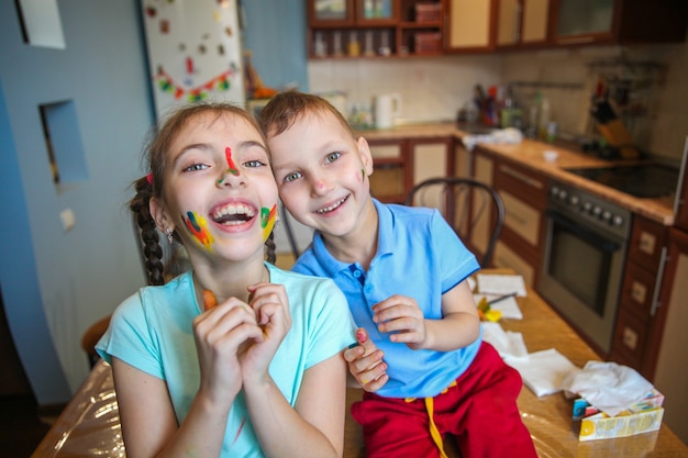 Embadurnado en pintura niños un niño y una niña tonteando y riendo en casa en la cocina