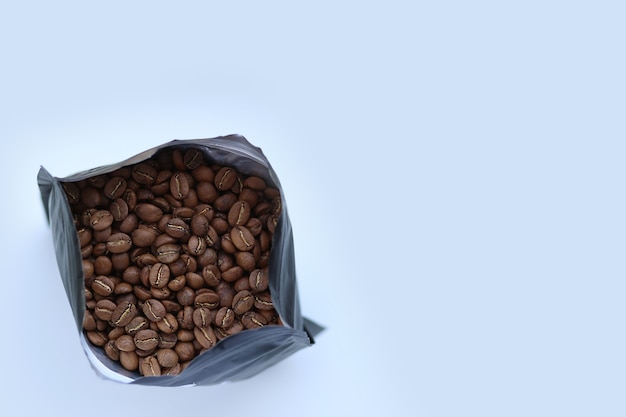 Embalado com grãos de café recém-torrados em um saco plástico preto na vista superior do fundo branco