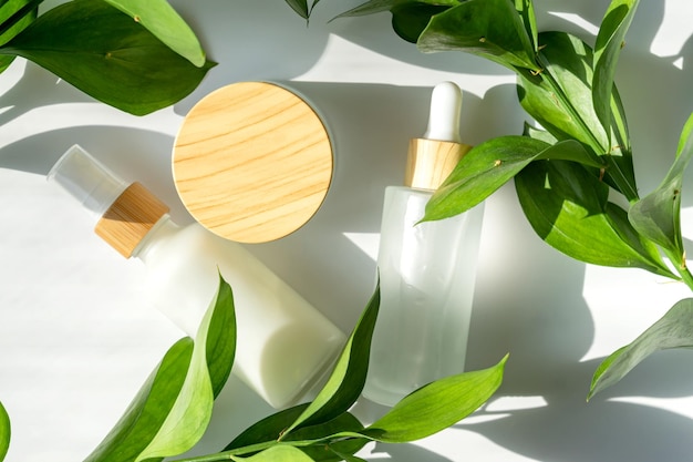 Embalagem de cosméticos Conjunto de diferentes garrafas cosméticas de creme ou soro em fundo branco com folhas verdes Embalagem em branco Conceito de produto de spa de beleza natural Mockup de beleza