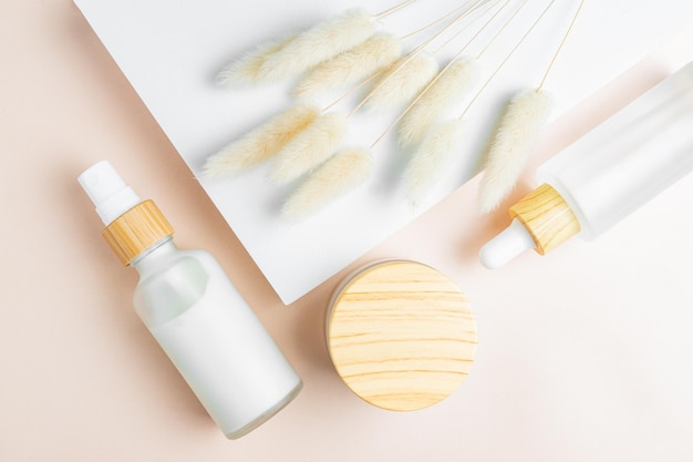 Embalagens de cosméticos Conjunto de diferentes frascos cosméticos de creme ou soro no pódio branco com flores de lagurus Embalagem em branco Conceito de produto de spa de beleza natural Maquete de beleza