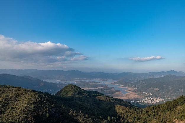 El embalse bajo el cielo azul y las nubes blancas está rodeado de montañas y bosques.