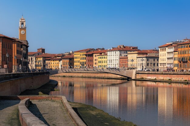 Embankment mit alter Stadtbrücke und Gebäuden und Reflexionen im ruhigen Wasser an einem sonnigen Tag Pisa Italien