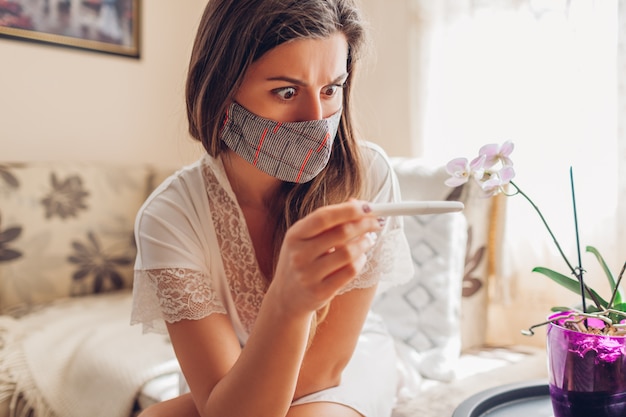 Embarazada durante el coronavirus covid-19. Mujer enferma en máscara comprobando la prueba de embarazo en casa.