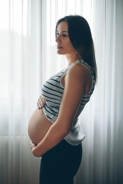 Embarazada sosteniendo su barriga desnuda frente a una cortina