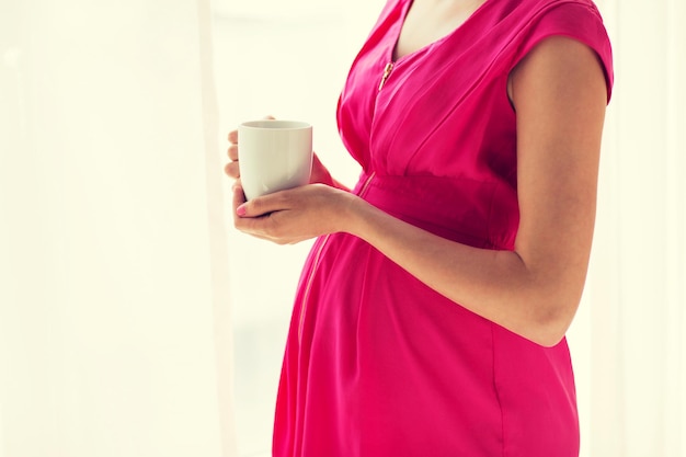 Embarazo, bebidas, descanso, personas y concepto de expectativa: cierre de una mujer embarazada con una taza de té en casa