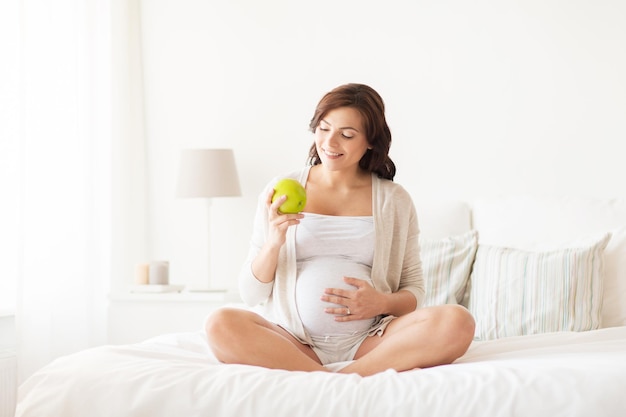 embarazo, comida saludable y concepto de personas - mujer embarazada feliz comiendo manzana verde en casa