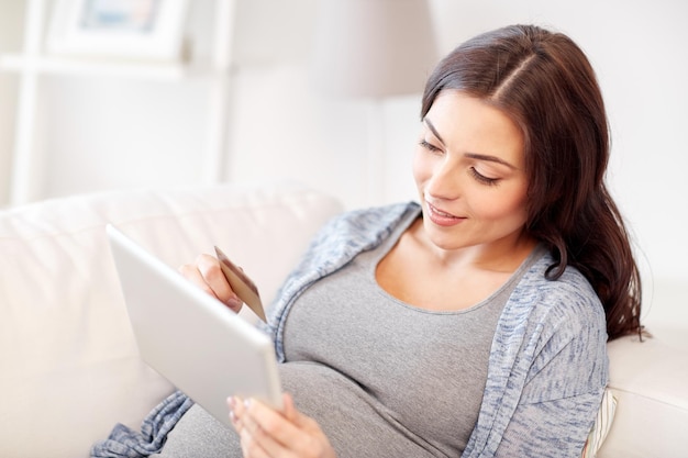 embarazo, compras en línea, tecnología y concepto de personas - mujer embarazada feliz con computadora de tablet pc y tarjeta de crédito en casa