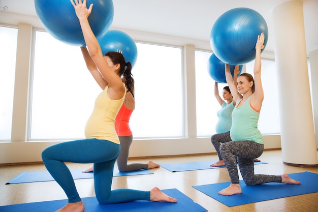 embarazo, deporte, fitness, personas y concepto de estilo de vida saludable - grupo de mujeres embarazadas felices haciendo ejercicio con pelota en el gimnasio