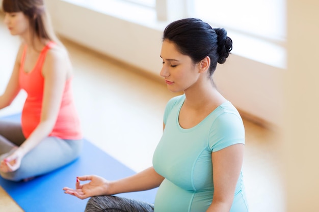 embarazo, deporte, fitness, personas y concepto de estilo de vida saludable - grupo de mujeres embarazadas felices haciendo yoga y meditando en pose de loto en el gimnasio