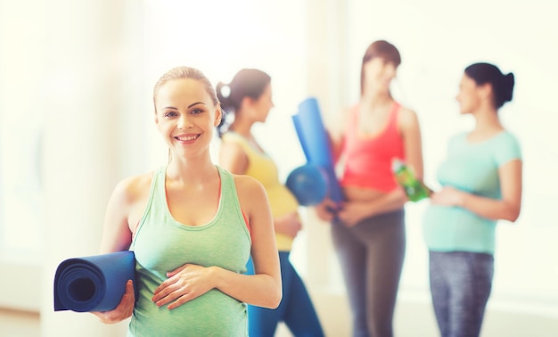 embarazo, deporte, fitness, personas y concepto de estilo de vida saludable - mujer embarazada feliz con alfombra en el gimnasio