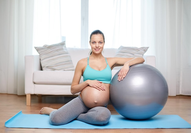 embarazo, deporte, fitness, personas y concepto de estilo de vida saludable - mujer embarazada feliz haciendo ejercicio con fitball en casa