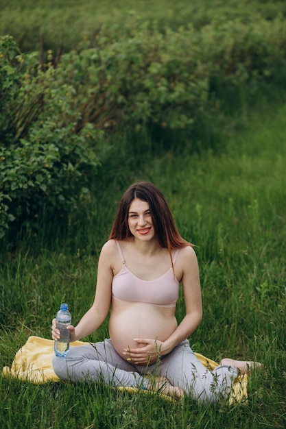 Embarazo deporte y salud estilo de vida mujer embarazada feliz bebiendo agua de un vaso en el parque en un día soleado de verano