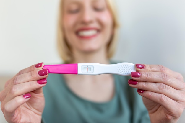 Embarazo fertilidad maternidad y personas concepto mujer sonriente feliz mirando la prueba de embarazo en casa