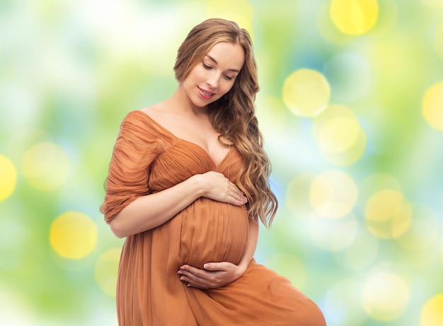 embarazo, maternidad, gente y concepto de expectativa - mujer embarazada feliz tocando su gran barriga sobre el fondo de luces verdes de verano