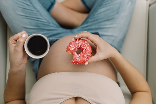 Embarazo y nutrición. Mujer embarazada disfrutando de té y donuts. Concepto de expectativa y salud.