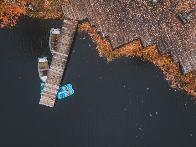 Embarcadero de la vista aérea con los barcos de madera en la orilla de un lago pintoresco, bosque del otoño. San Petersburgo, Rusia.