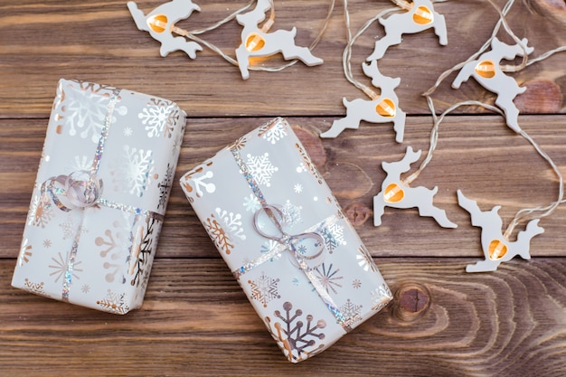 Embrulhado em caixas de presente de embalagem festiva amarradas com fita de prata e guirlanda de veados de natal em uma mesa de madeira. preparando para o natal.