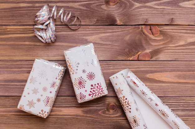 Foto embrulhado em caixas de presente de embalagem festiva, fita e rolo de papel de embrulho em uma mesa de madeira. preparando para o natal.