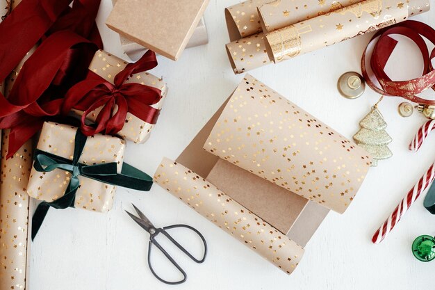 Embrulhando elegante presente de natal plana lay caixas de presente modernas fitas vermelhas e verdes enfeites de papel de embrulho dourado e tesoura em fundo branco feliz natal inverno atmosférico