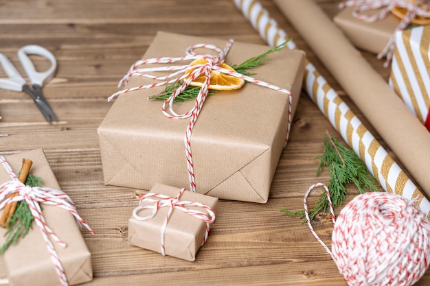 Embrulhar presente de natal perto de presentes não preparados em fundo de madeira com canela laranja